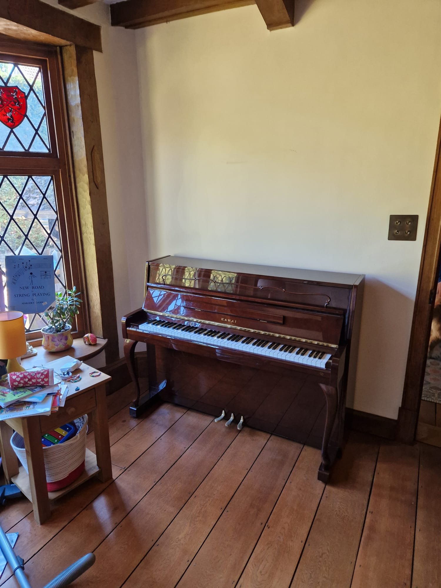 Compact upright piano beside a stained glass window in a wooden-floored room.
