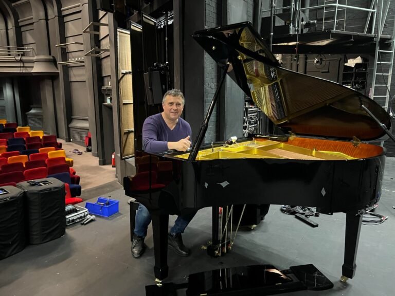Piano technician seated beside grand piano on a theatre stage