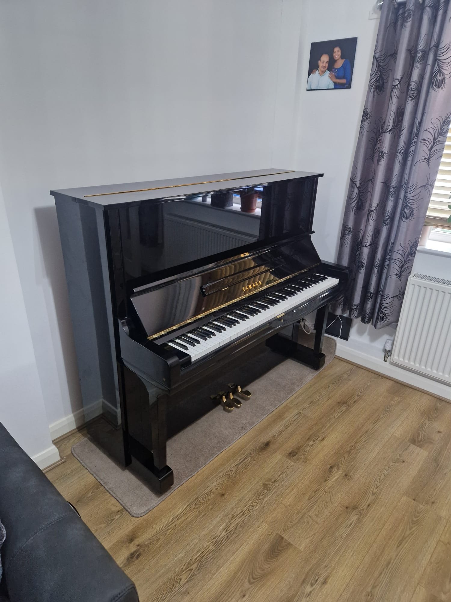 Black upright piano placed in a modern home on a light wood laminate floor.