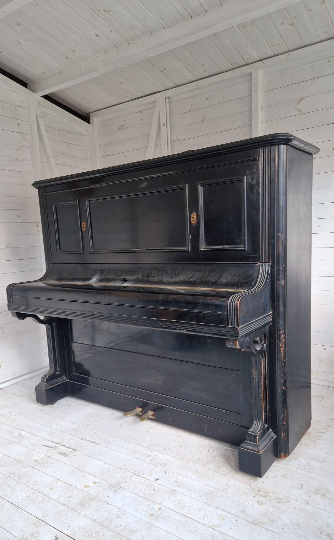 Aged upright piano with worn finish, positioned in a storage area.