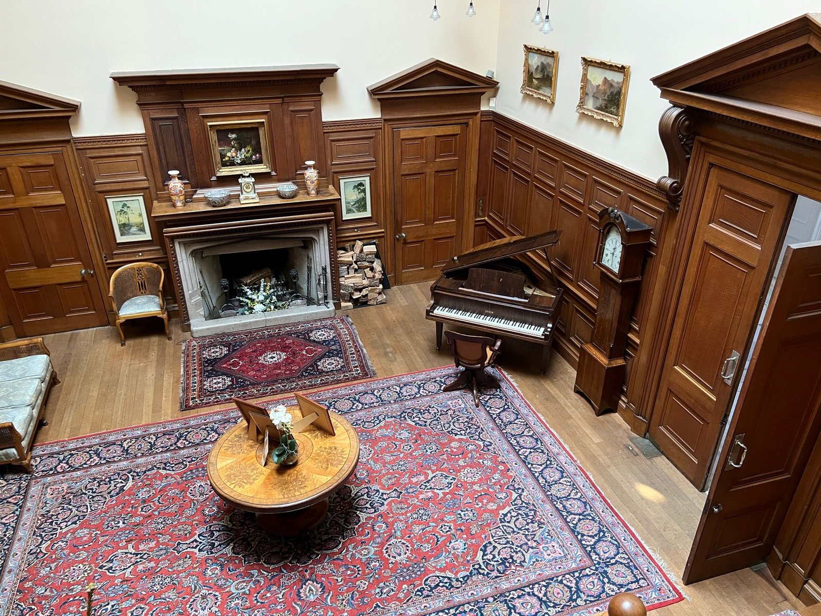 Victorian-style living room with upright piano and ornate furniture on a red oriental rug.